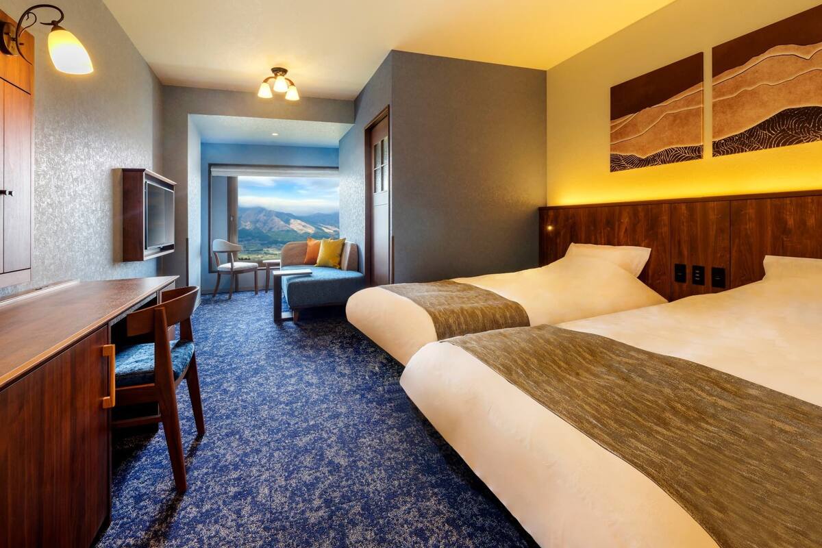 Ein Hotelzimmer mit Bett, Schreibtisch, Stuhl, Fernseher und Blick auf Berge.