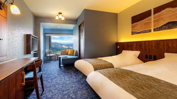 A hotel room with a bed, a desk, a chair, a TV, and a view of mountains.