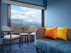 Une pièce comprenant un canapé, deux fauteuils, une petite table et une grande fenêtre donnant sur une vue sur les montagnes.