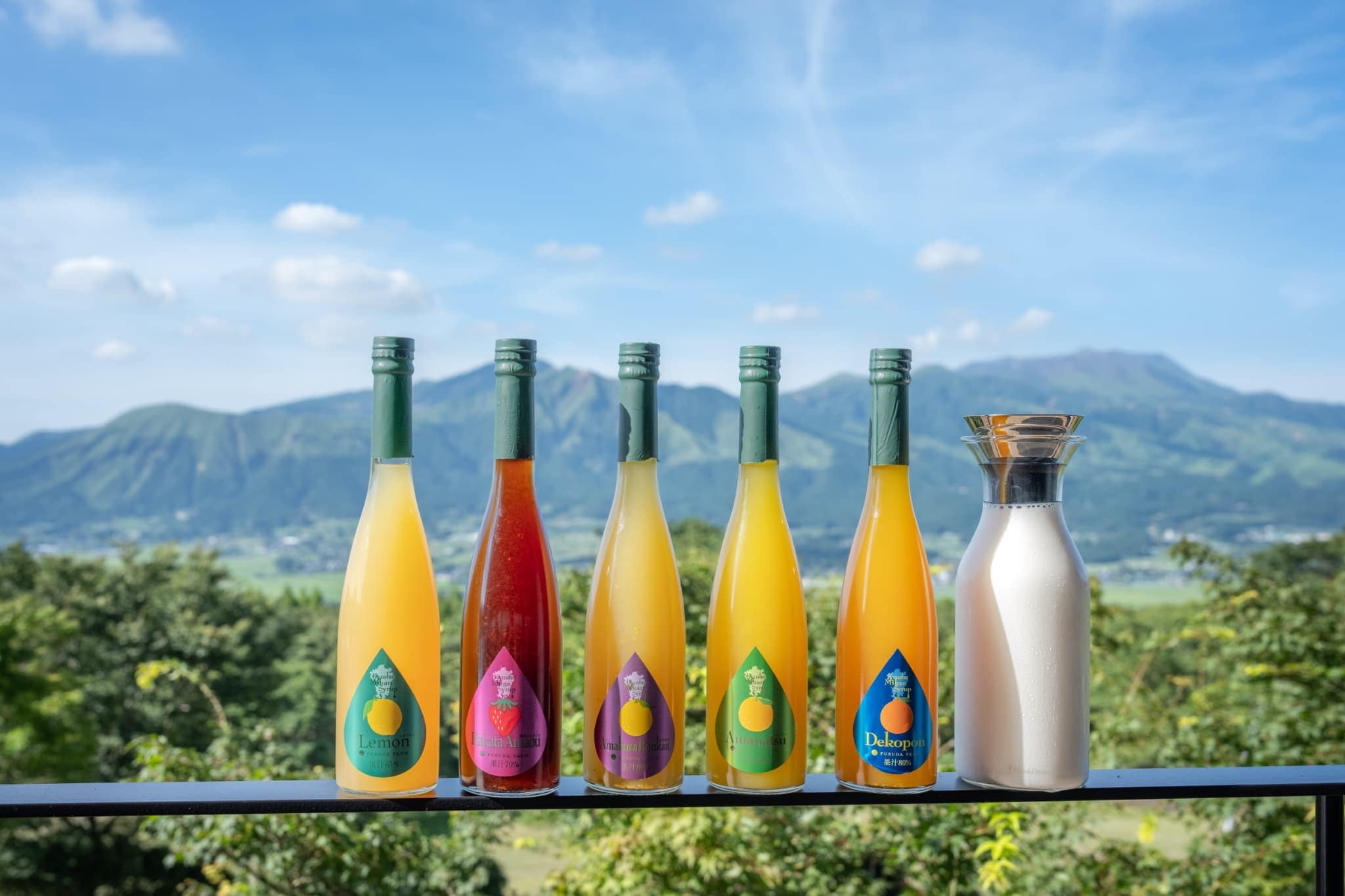 A row of colorful bottles with labels, set against a backdrop of a mountainous landscape.