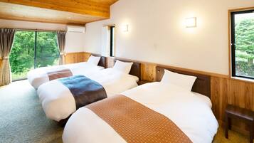 Habitación de hotel con tres camas, vigas de techo de madera, ventana con vista a follaje y aire acondicionado de pared.