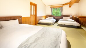 Een hotelkamer met twee bedden, houten hoofdeinden, een raam met gordijnen en uitzicht op groen.
