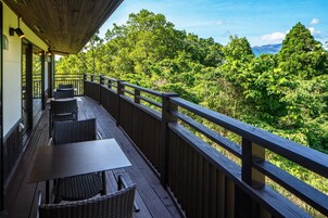 Terraza de madera con mobiliario exterior y vista a un bosque frondoso.
