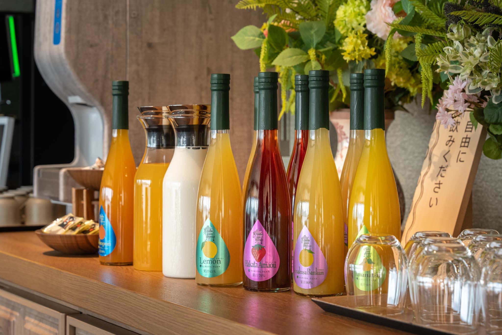 Variedad de botellas de bebidas sobre una encimera con fondo de madera y una planta decorativa.