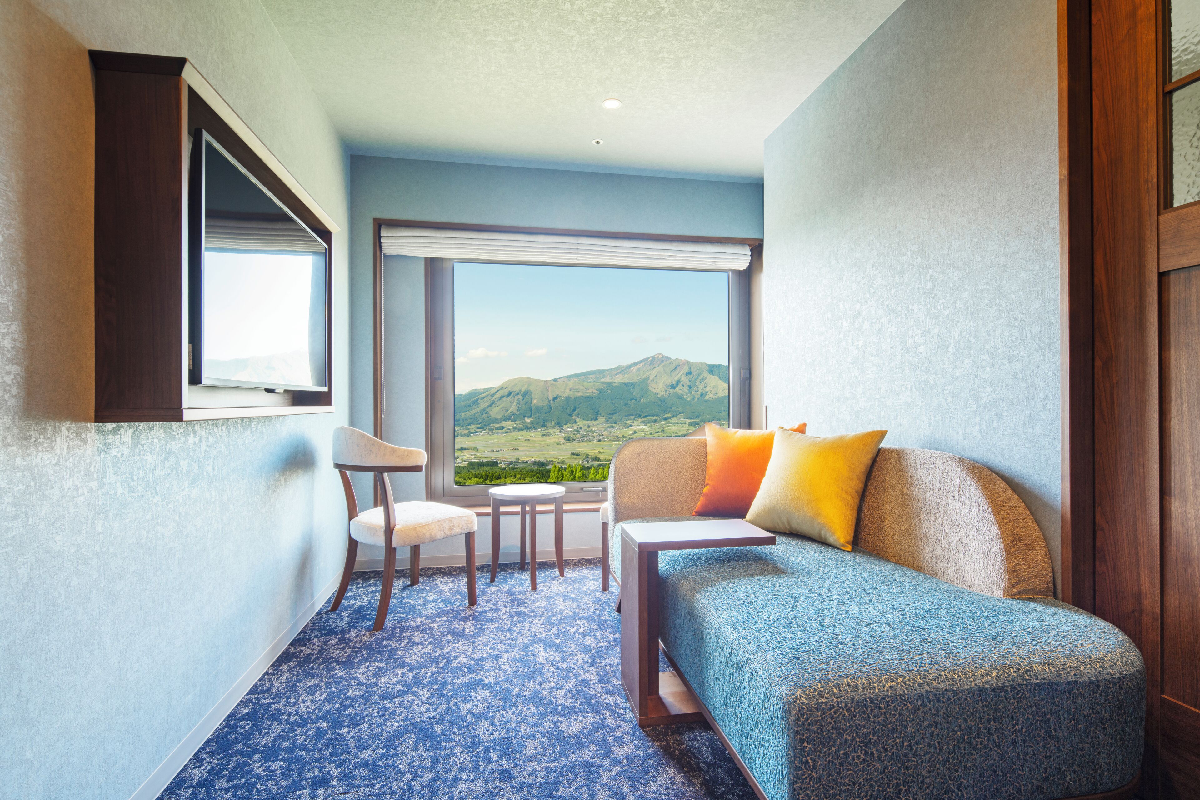 Una habitación de hotel con un ventanal grande, un sofá, una silla y una mesita.