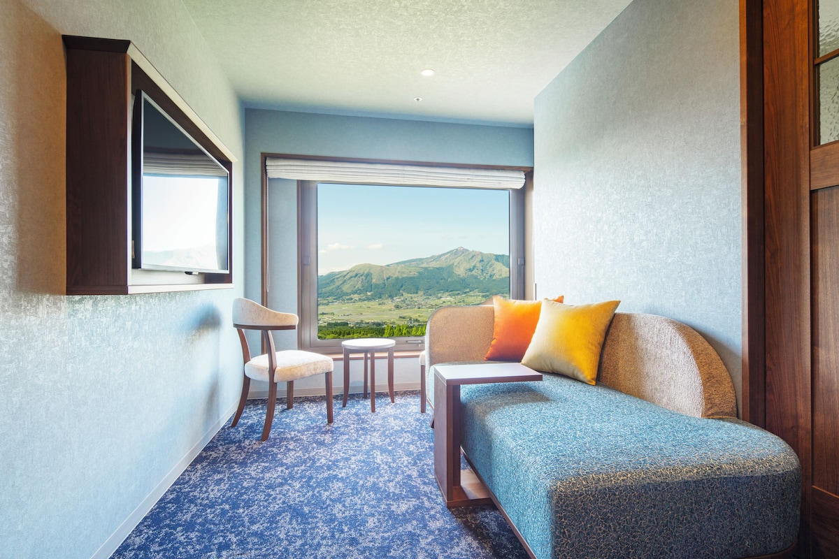 Ein Hotelzimmer mit großem Fenster, einer Couch, einem Sessel und einem kleinen Tisch.