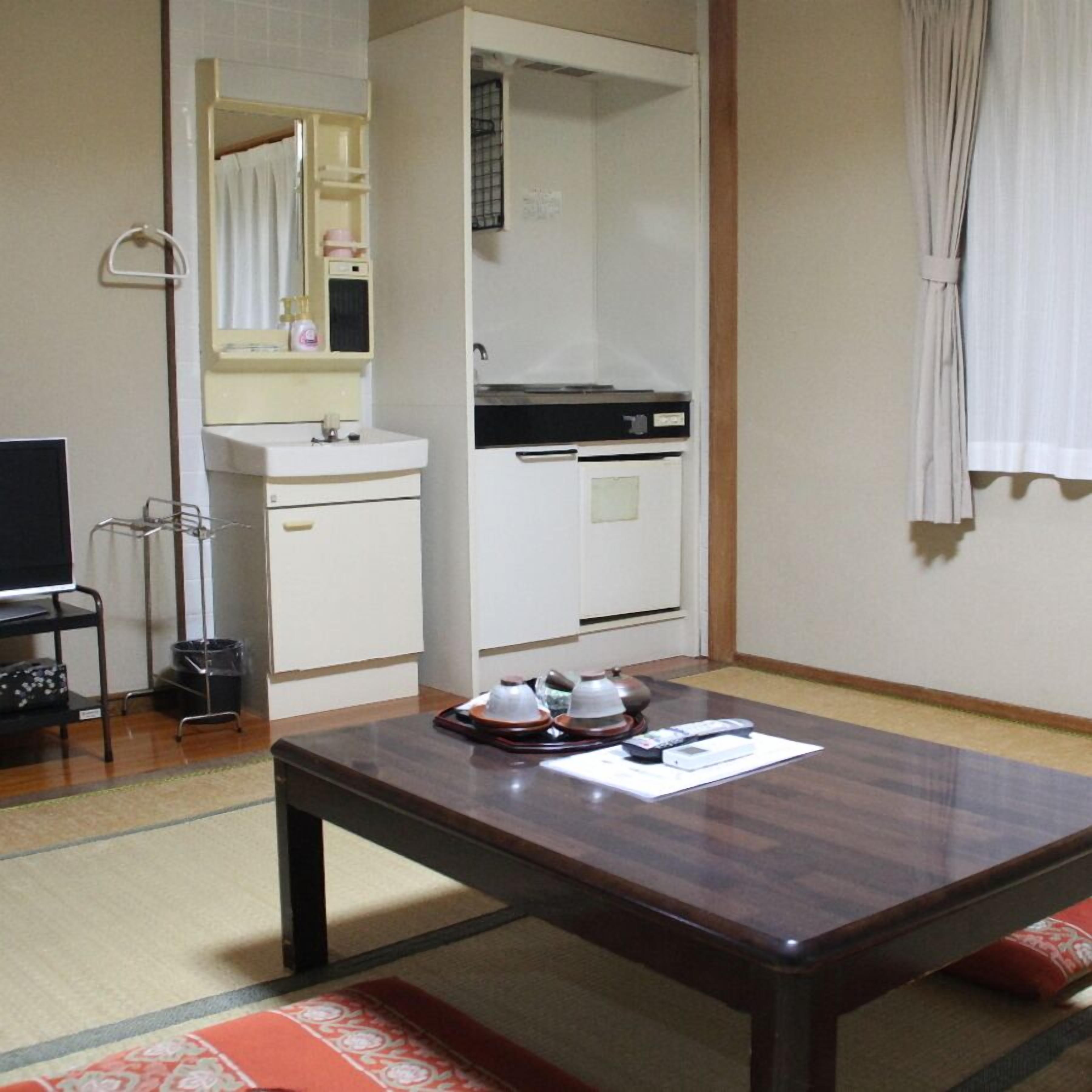 A hotel room with a wooden table, a television, a sink, and a wardrobe.
