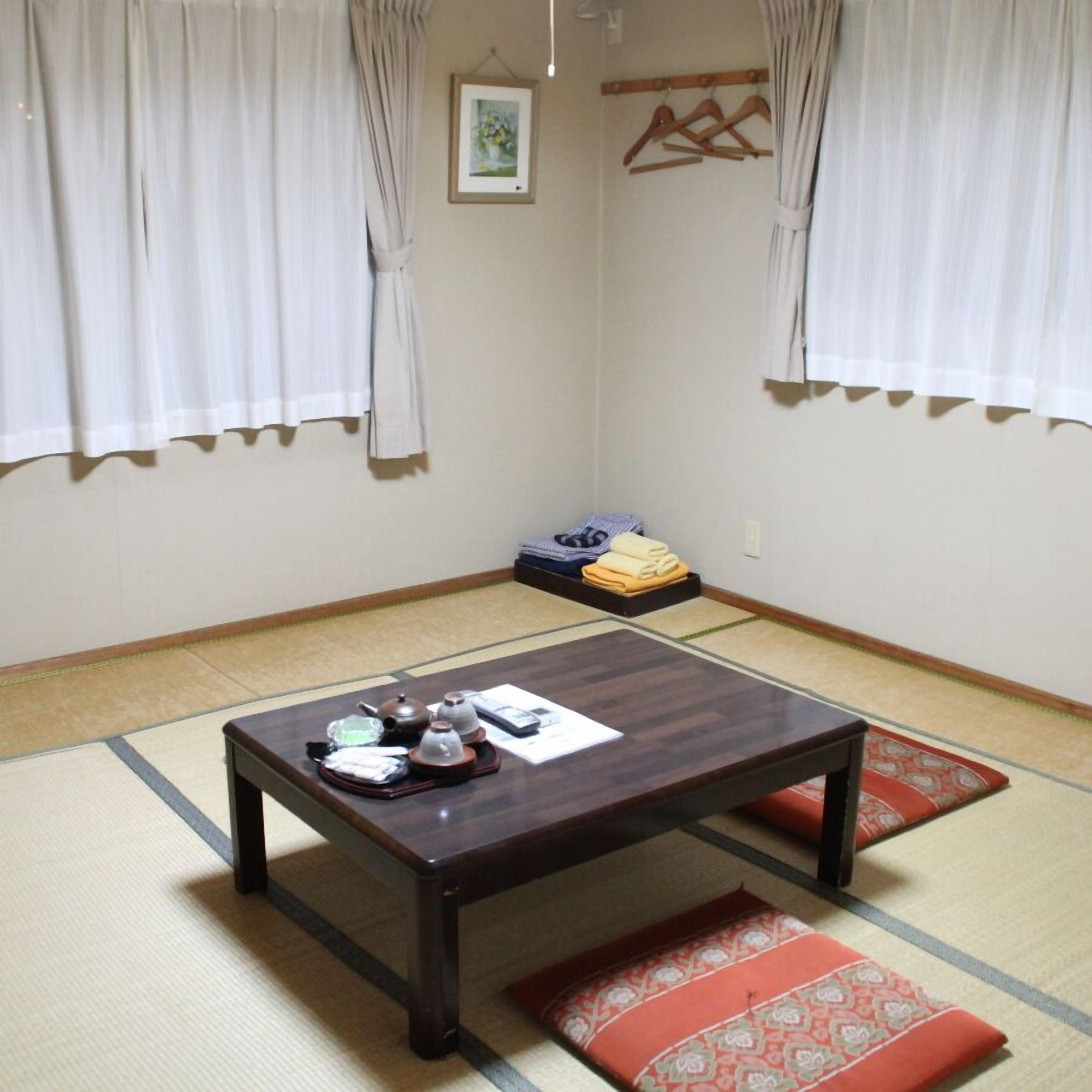 A traditional Japanese room with tatami flooring, a dark wooden table with tea set, and a futon bed.