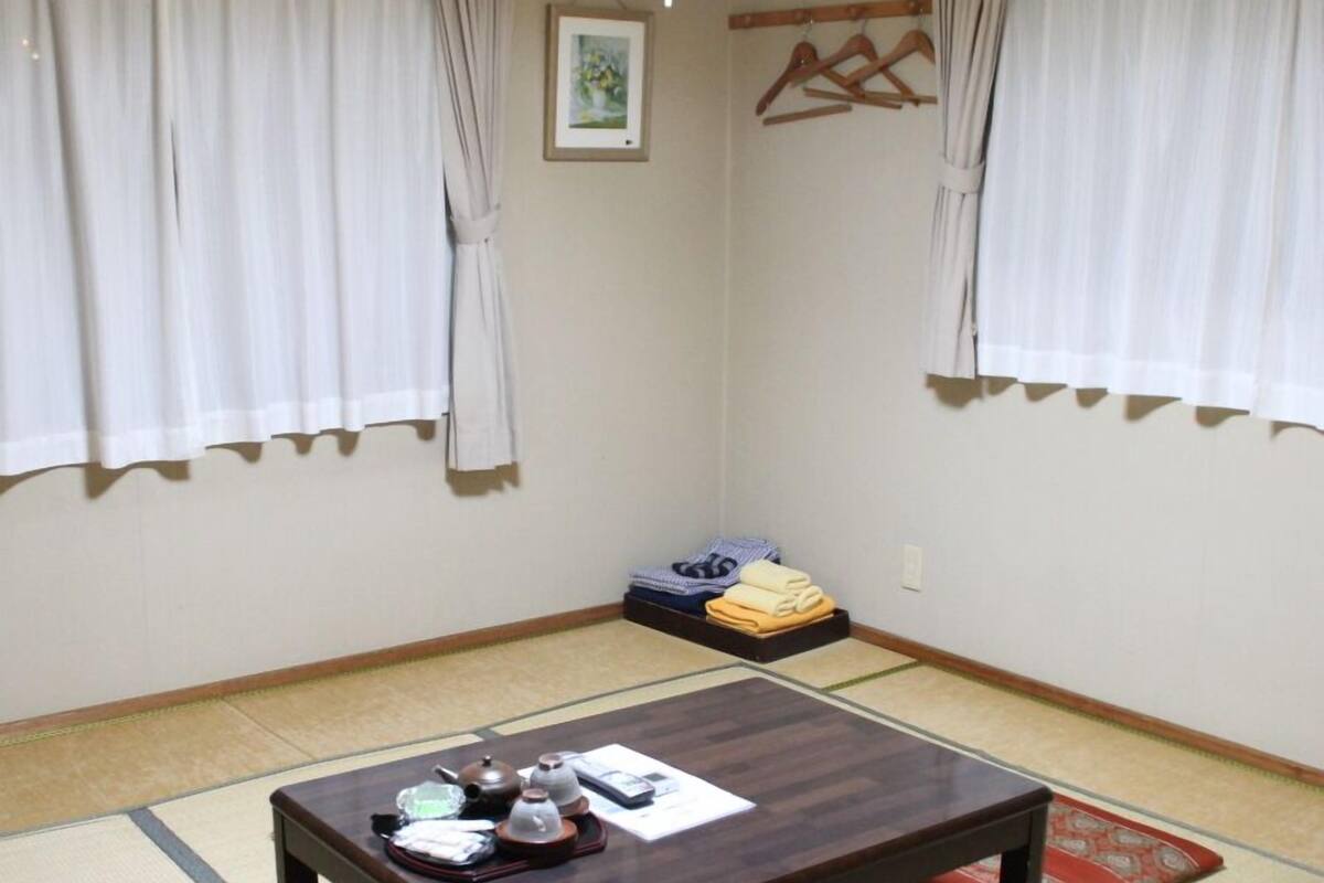 Une pièce de style japonais traditionnel, avec un sol recouvert de tatamis, une table en bois foncé agrémentée d’un service à thé et un futon servant de lit.