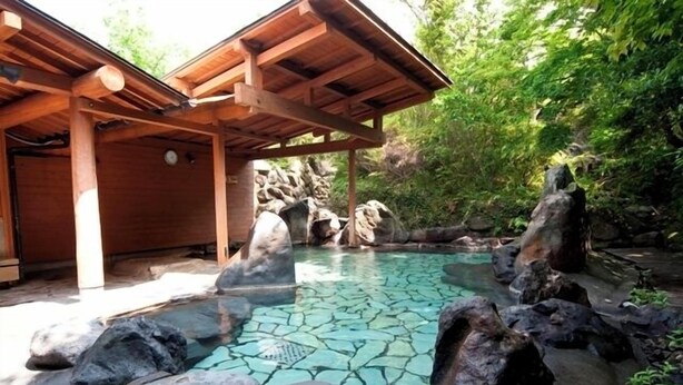 Un pabellón de madera con una piscina de azulejos rodeada de rocas y follaje.