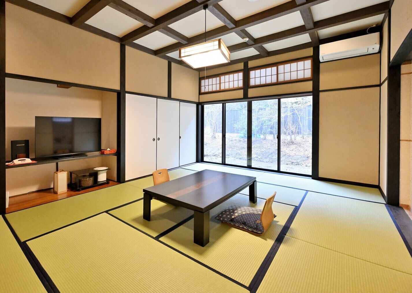 Una habitación tradicional japonesa con tatami, una televisión, un bajo mesa y puertas correderas.