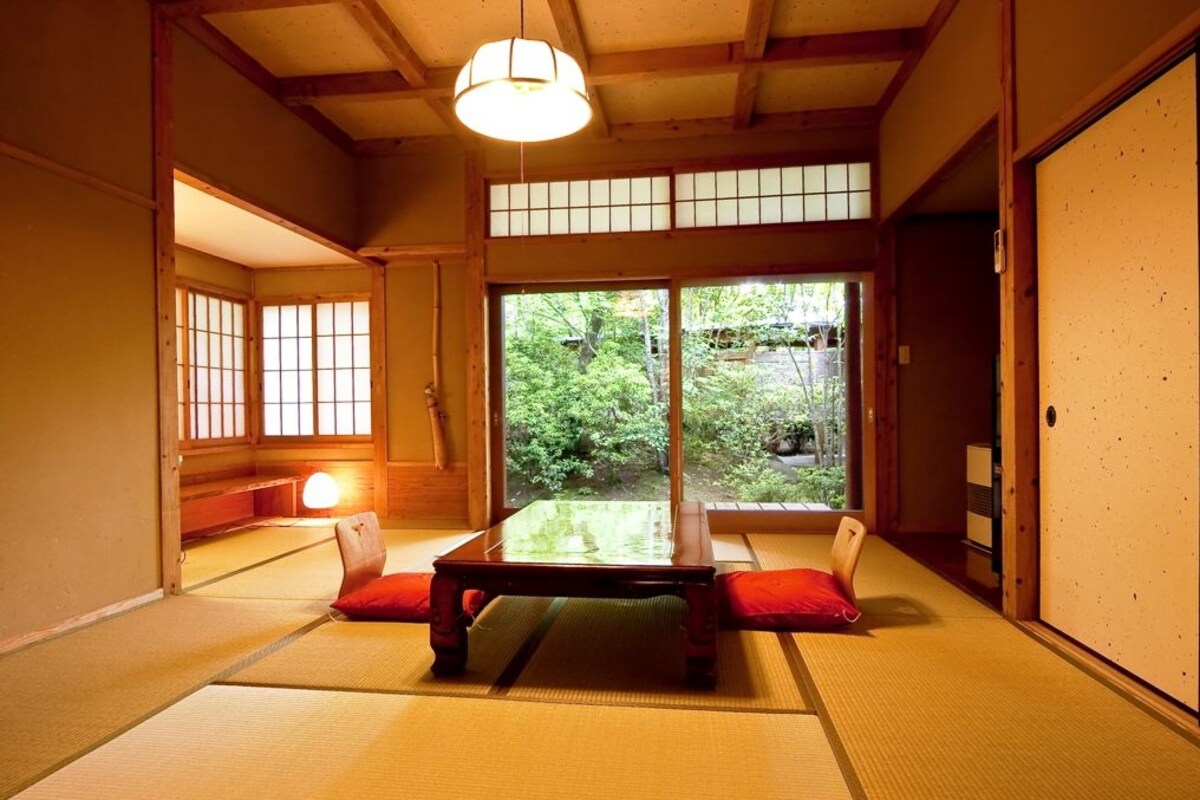 A traditional Japanese room with tatami flooring, a low wooden table, and sliding doors leading to a garden.