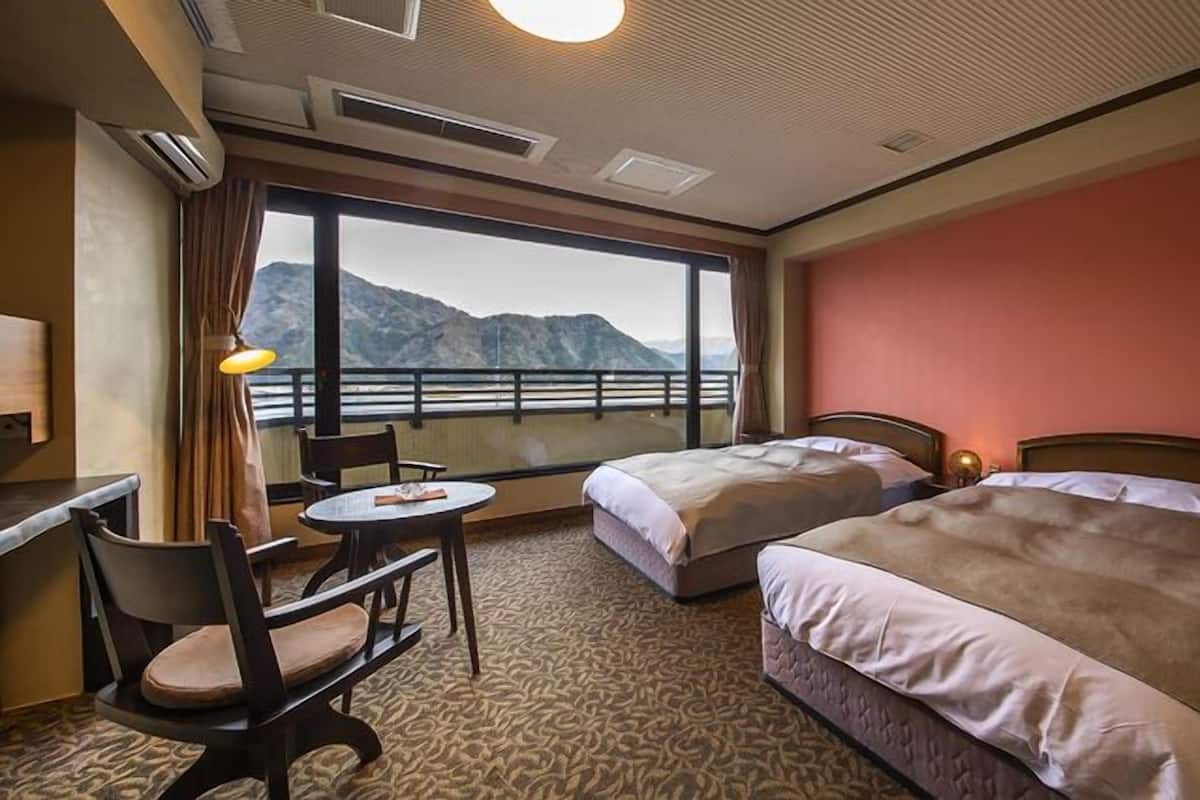 Ein Hotelzimmer mit zwei Betten, einem Schreibtisch, einem Stuhl und einem Fenster mit Bergblick.