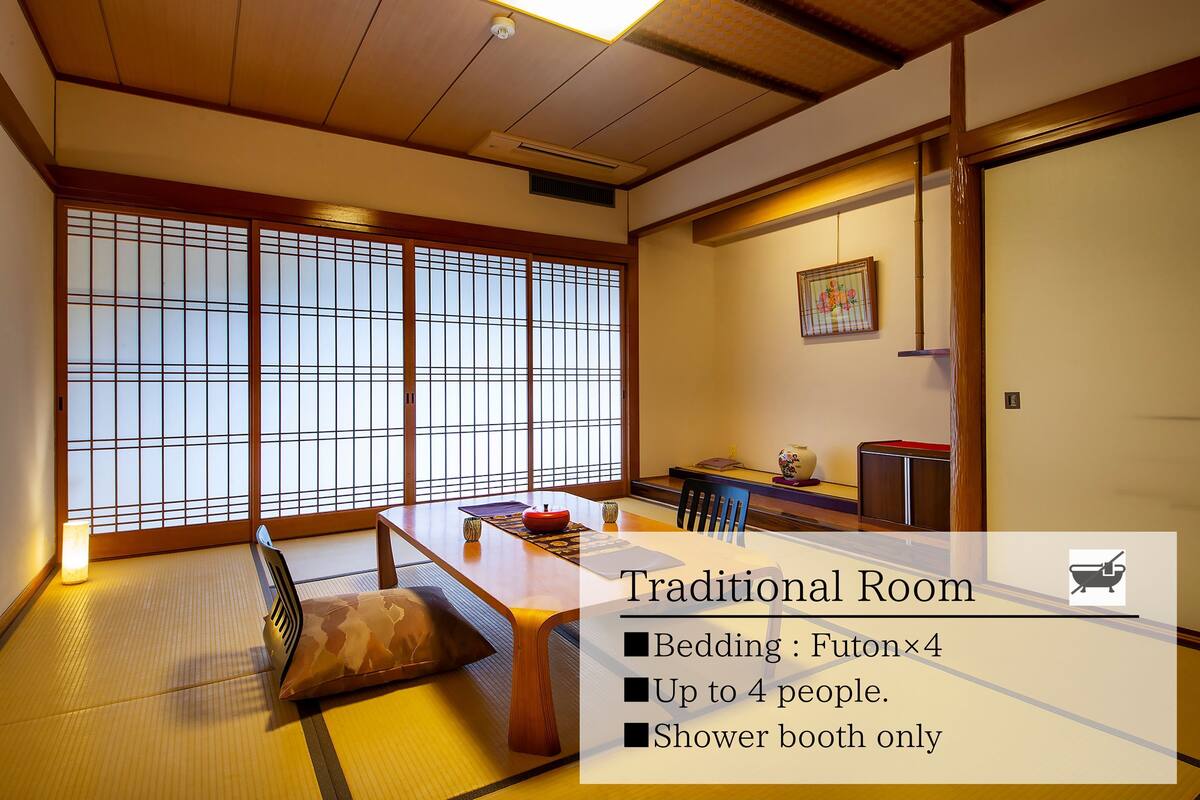 Ein traditioneller japanischer Raum mit Tatami-Boden, einer Futon-Liege, einem Esstisch und einer Schiebetür mit Blick.