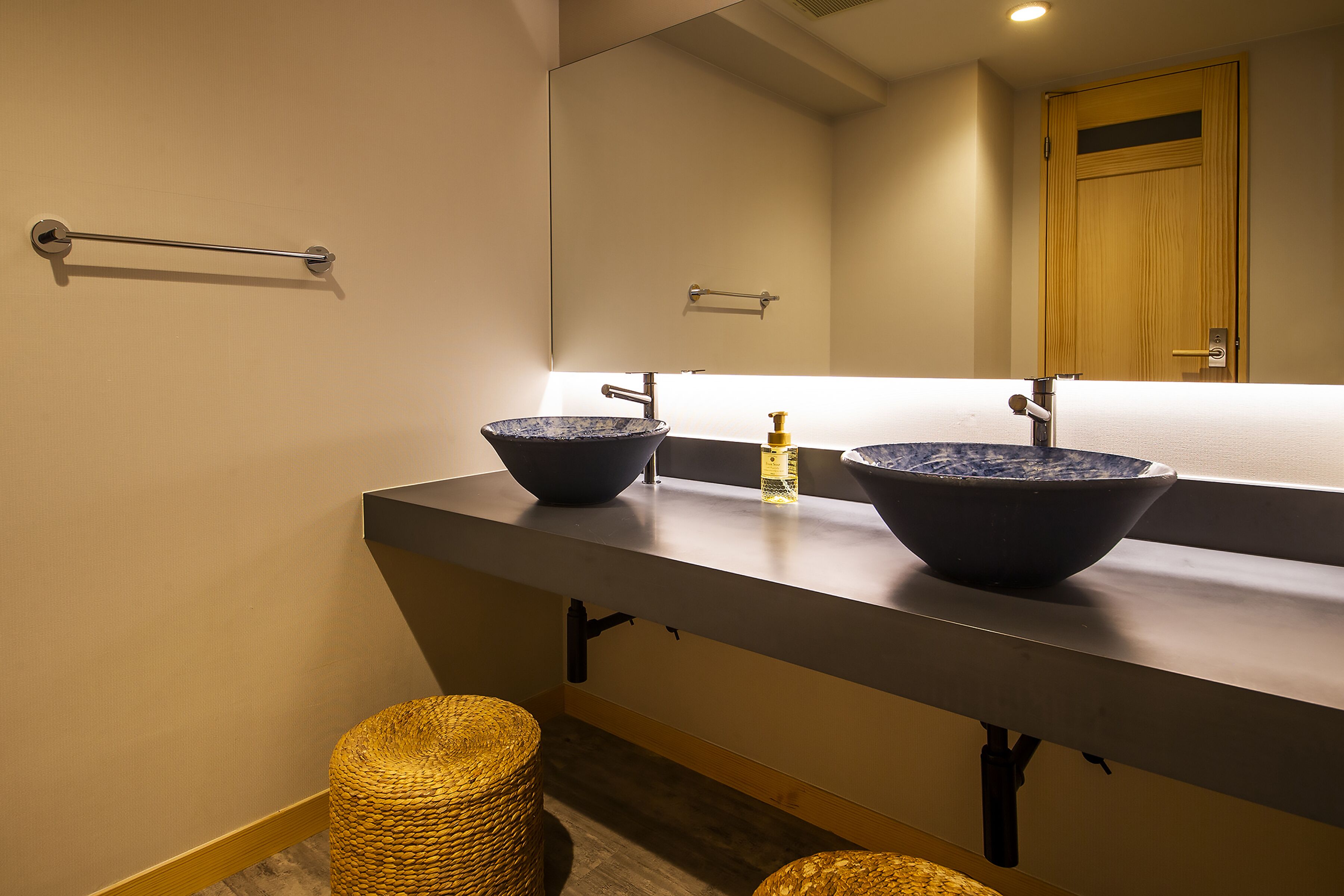 Un baño con dos grandes recipientes como lavamanos, un espejo, un perchero para toallas y una puerta de madera.