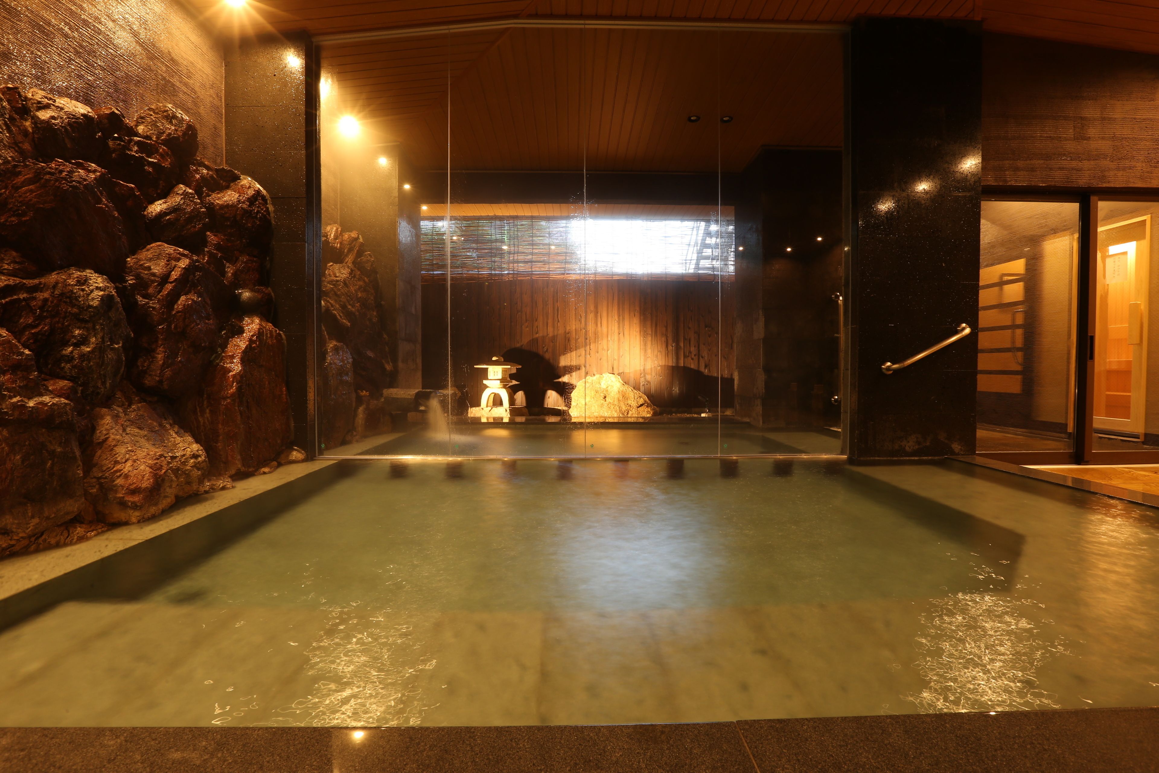 A spa area with a hot spring, wooden wall, and a stone wall with rocks.