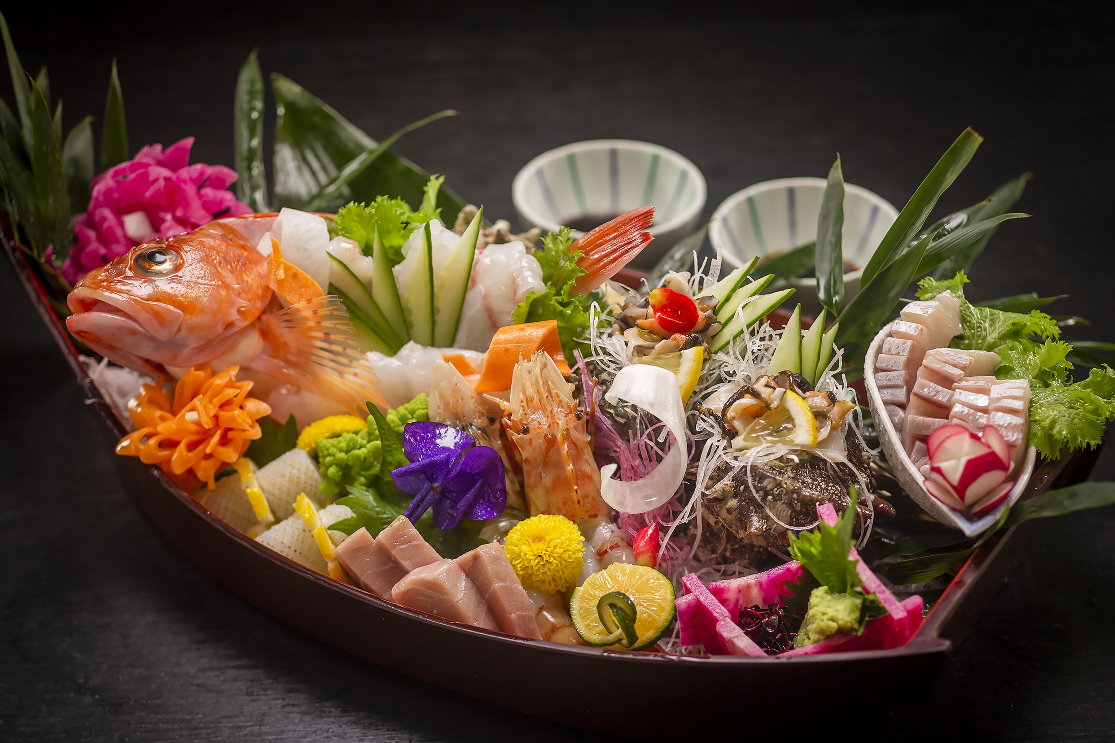 Variedad de mariscos dispuesta en un plato decorativo, que incluye pescado, camarones y otras exquisiteces marinas, acompañada de vegetales frescos y adornos.