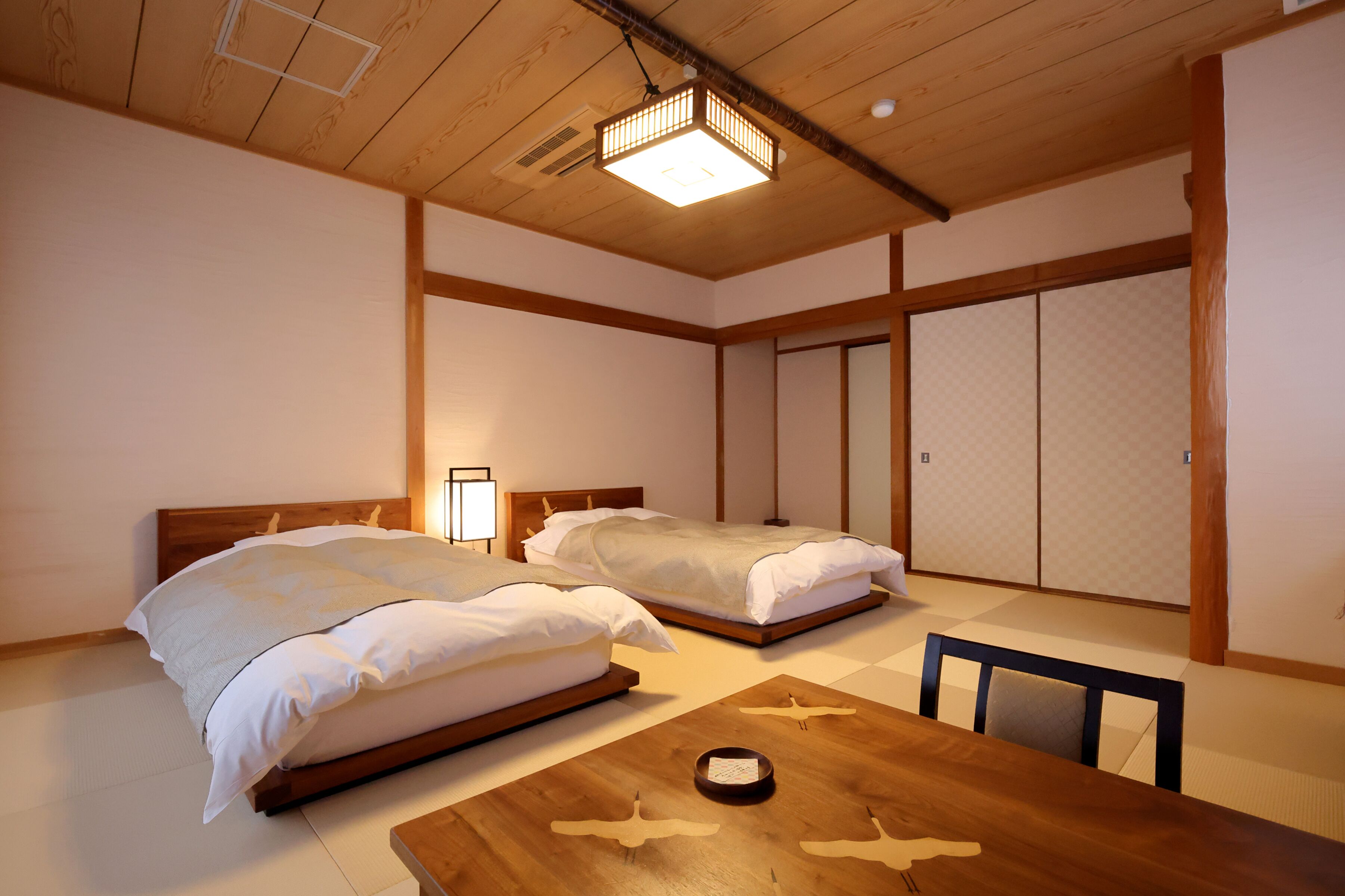 A traditional Japanese-style room with two wooden beds, tatami flooring, and sliding shoji doors.