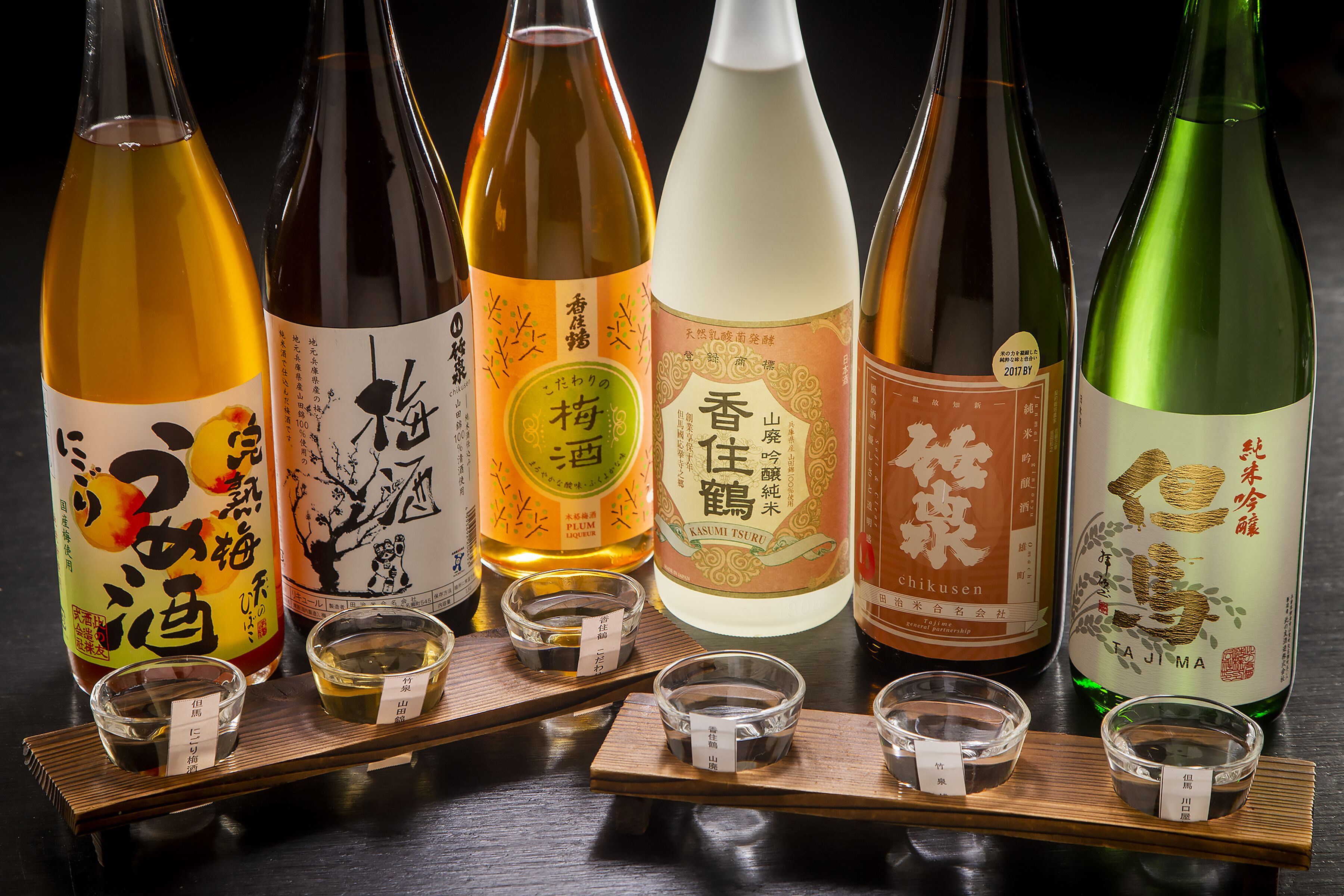 Varias botellas de sake y pequeños cuencos con sake sobre bandejas de madera.
