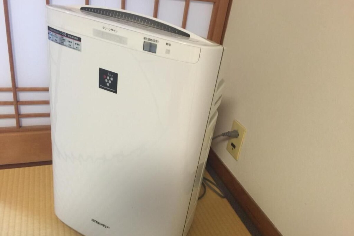 A white portable air conditioner with a control panel and a power cord plugged into a wall socket.