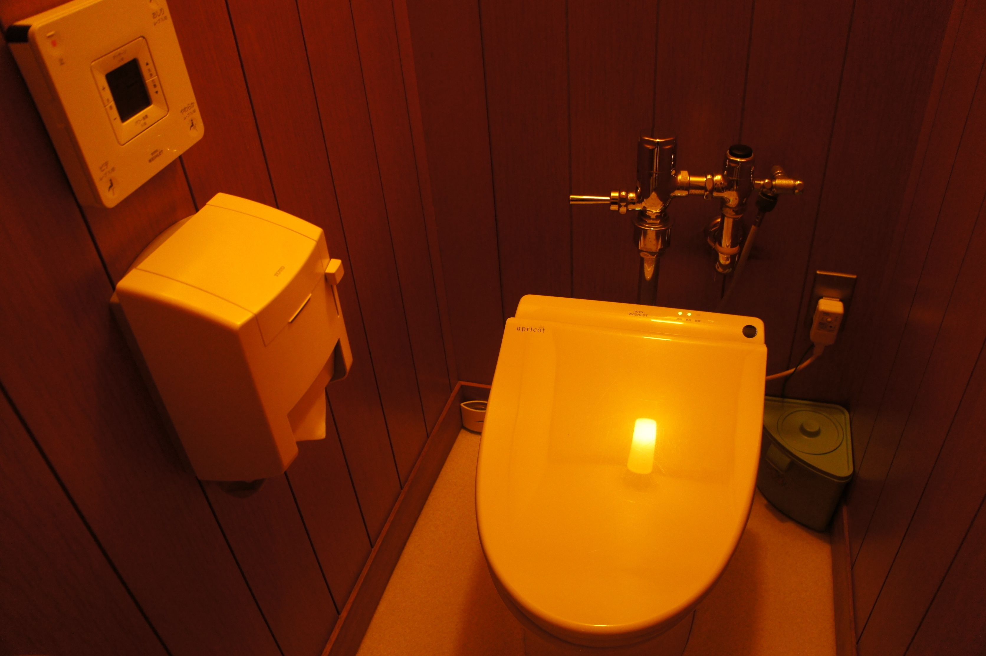 Une petite salle de bain compacte, dotée de toilettes blanches, d’un sèche-mains et d’un robinet de chasse d’eau fixé au mur.