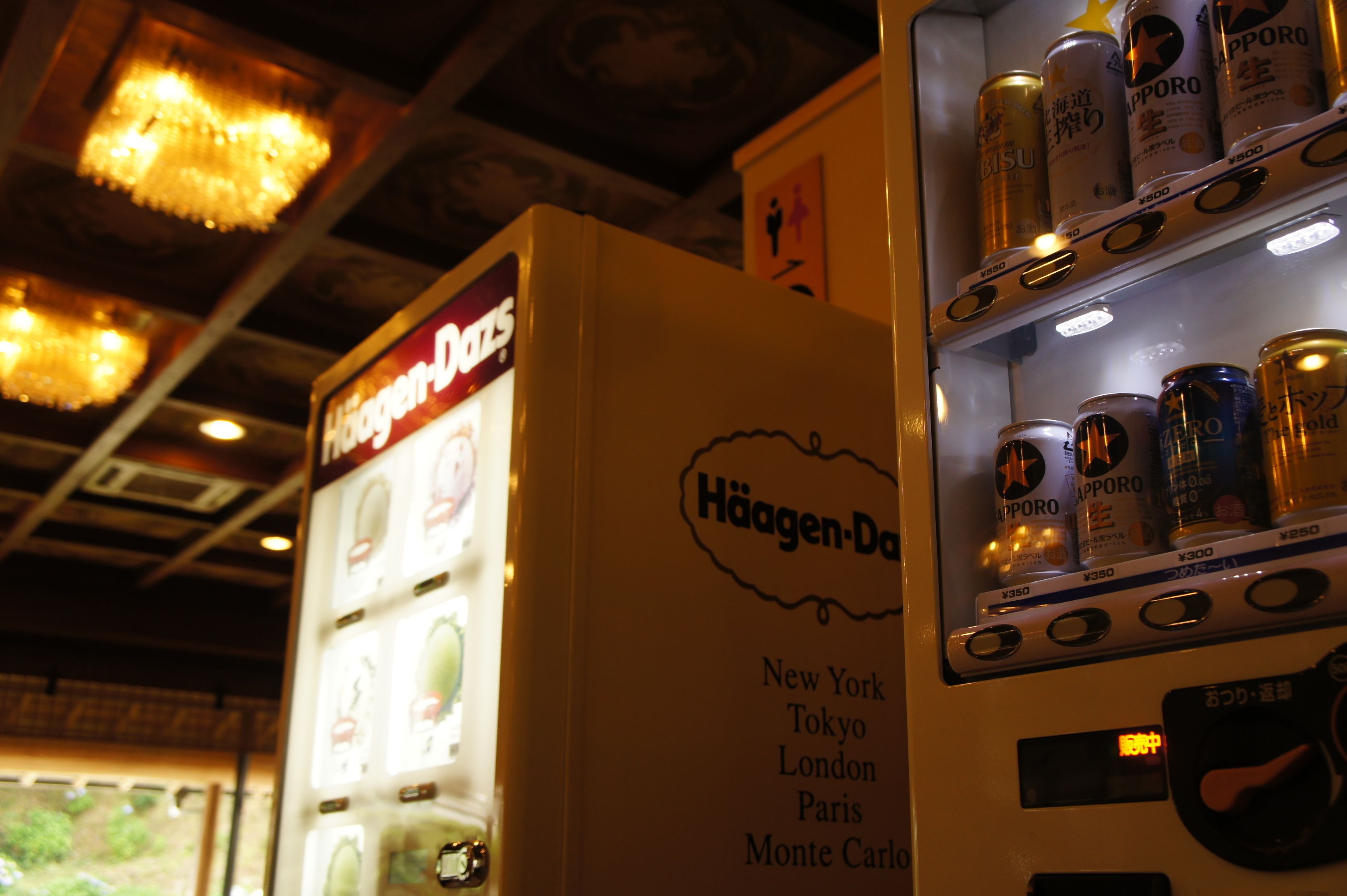 A vending machine with various drink cans, a sign for Häagen-Dazs, and a list of cities including New York, Tokyo, London, Paris, and Monte Carlo.