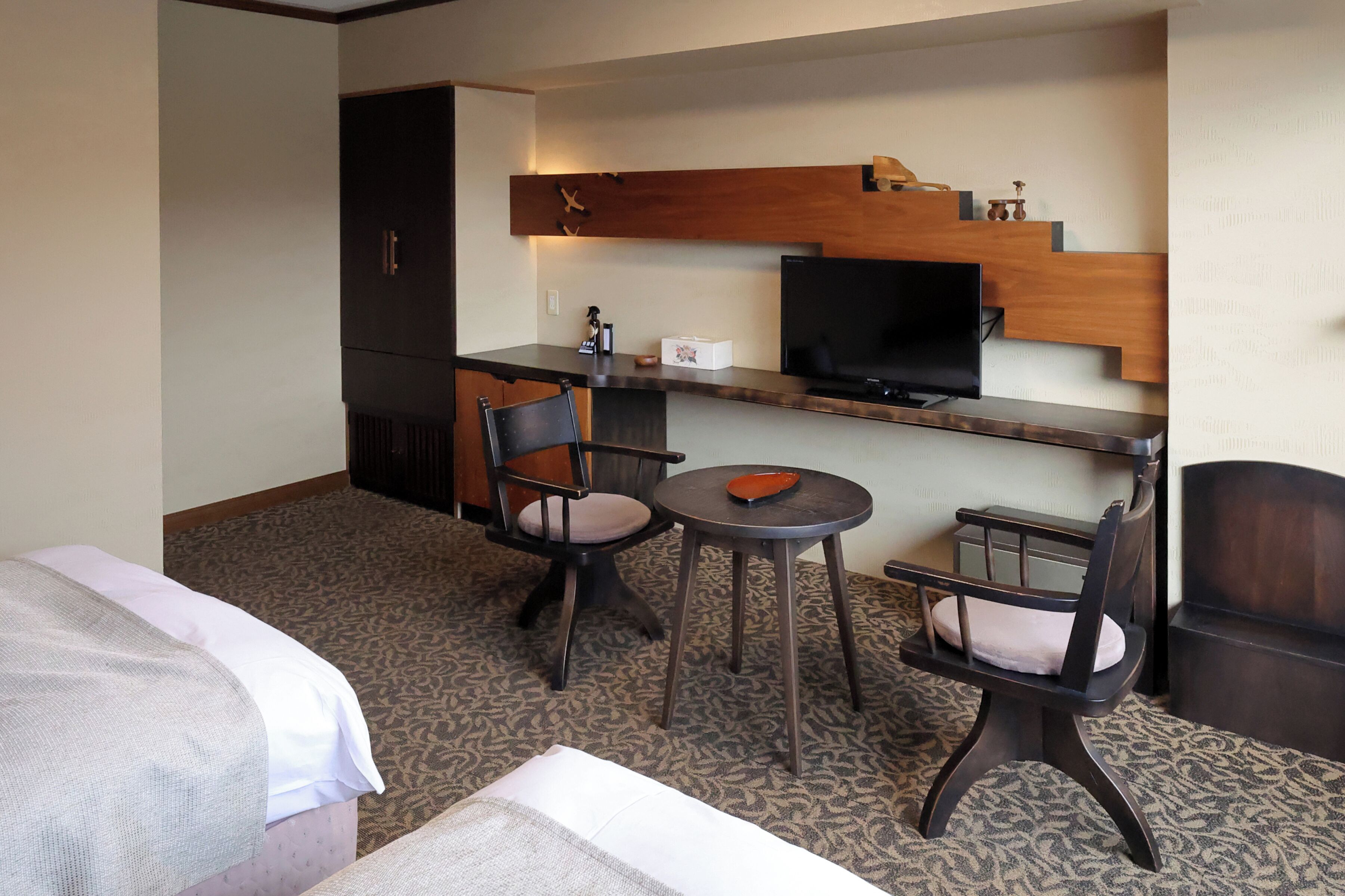 Une chambre d’hôtel comprenant un lit, un bureau, deux chaises, une télévision et une petite table.