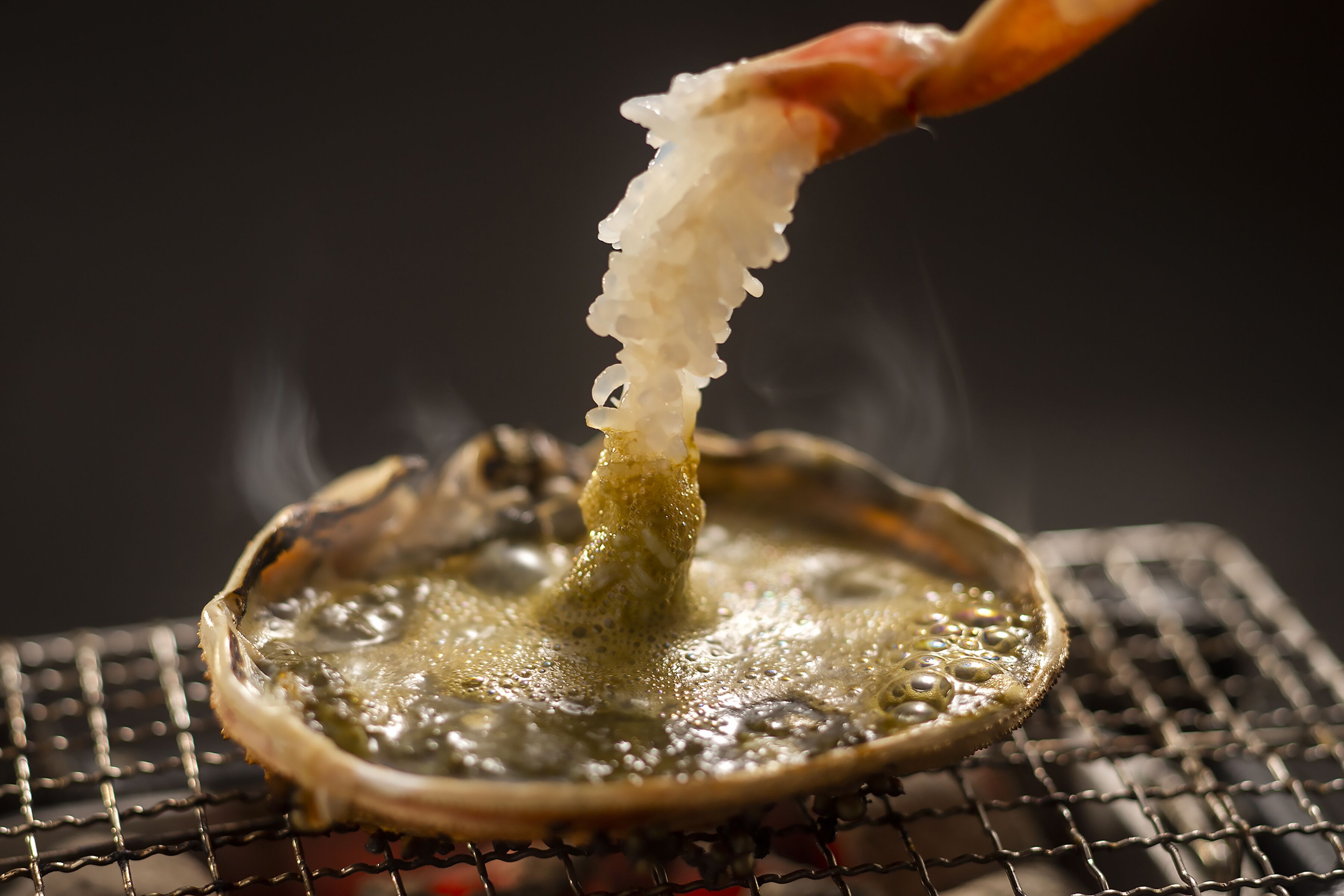 A close-up of a shrimp being dipped into a hot oil bath, likely for frying.