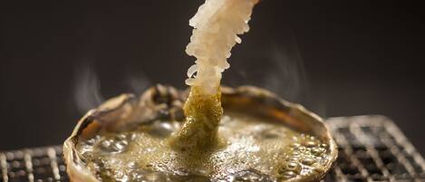 A close-up of a shrimp being dipped into a hot oil bath, likely for frying.