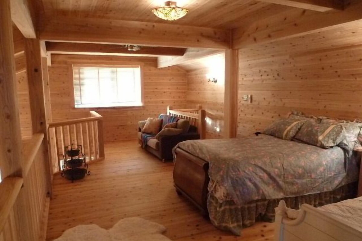 Un dormitorio acogedor estilo cabaña con piso de madera, una cama con ropa de cama estampada, un pequeño sofá y una ventana con persianas.