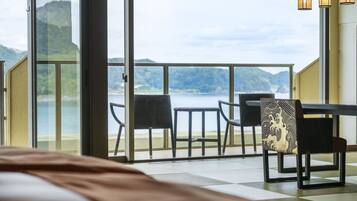 A balcony with a table and chairs overlooking a lake, with a bed in the foreground.