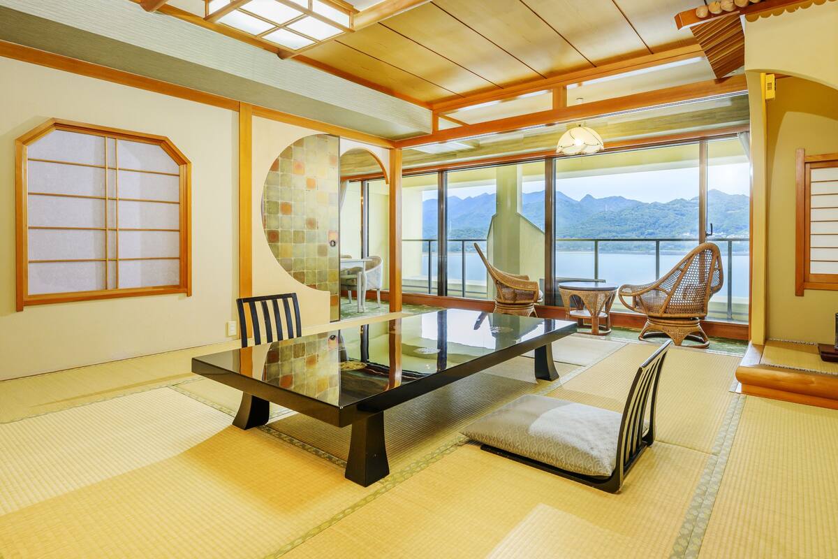 Ein traditioneller japanischer Raum mit Tatami-Boden, einem niedrigen Tisch und Blick auf Berge durch große Fenster.