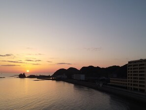 Ein Sonnenuntergang über einem ruhigen Fluss, im Hintergrund Gebäude und Hügel.