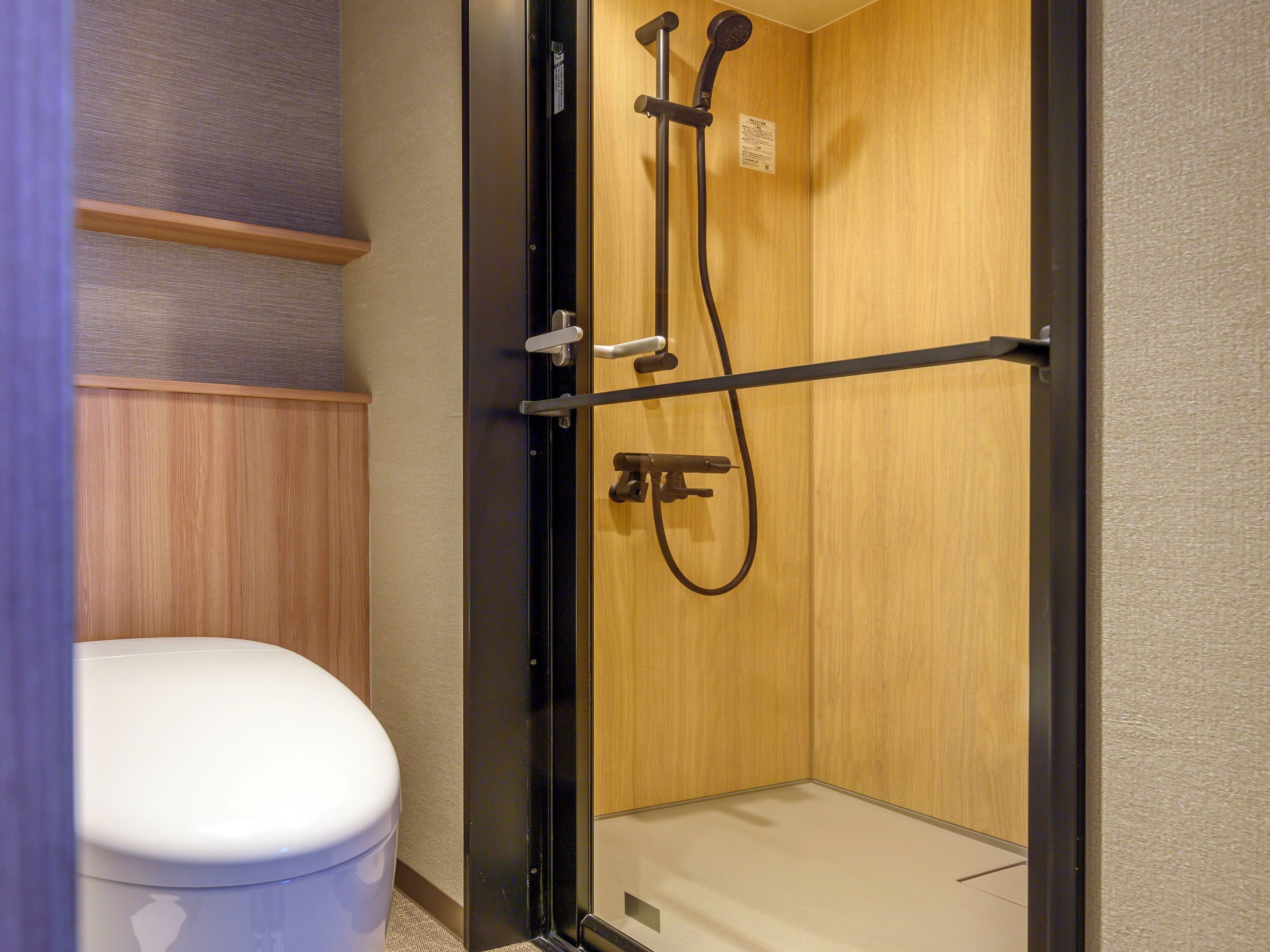 A walk-in shower with a wooden door and a toilet to the left.