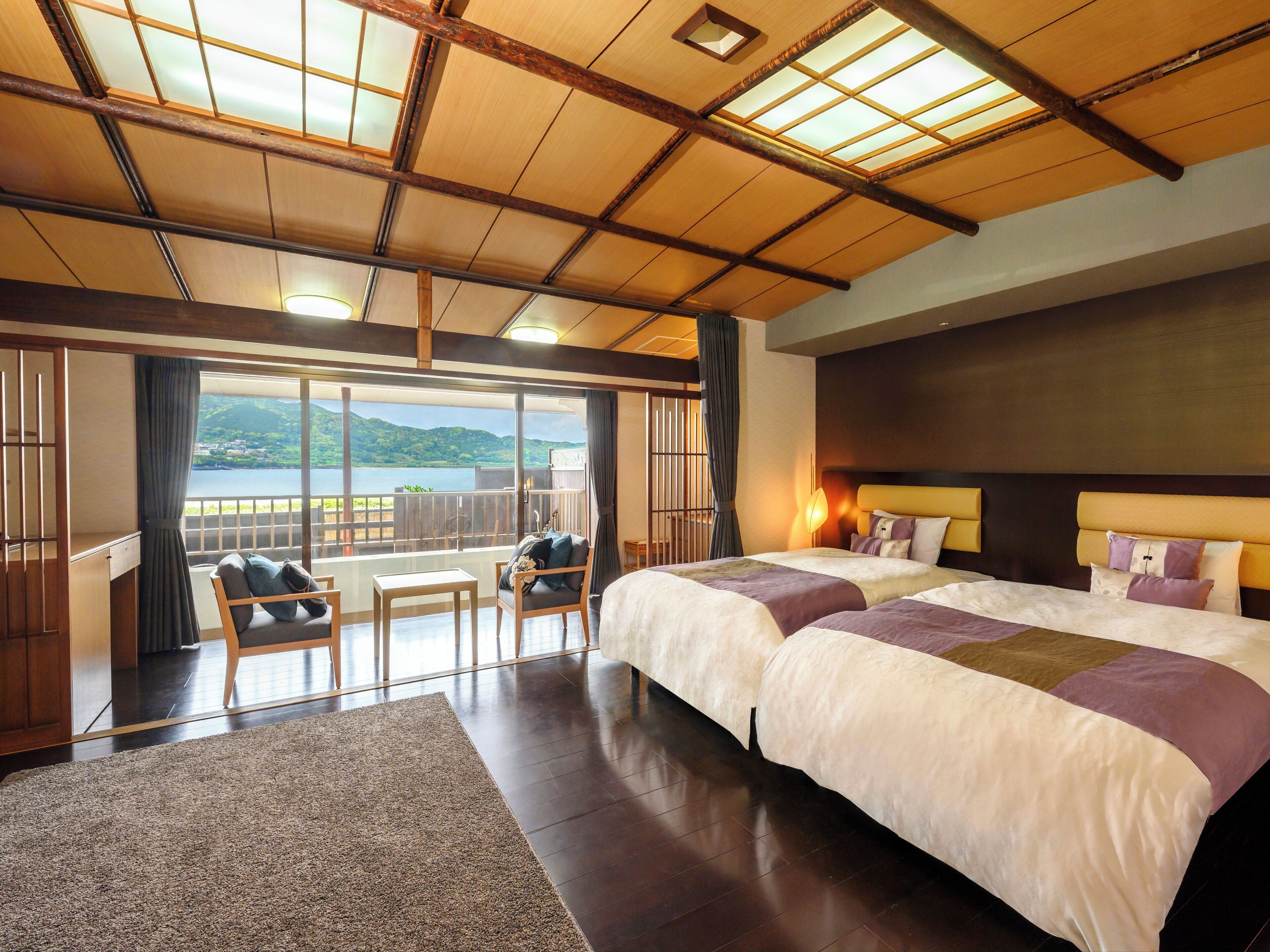 A hotel room with two beds, a balcony with a view of the sea, and a wooden ceiling.