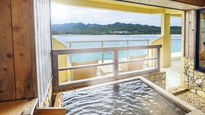 A hot spring bath area with a wooden bench and a stone wall, overlooking a body of water and mountains.