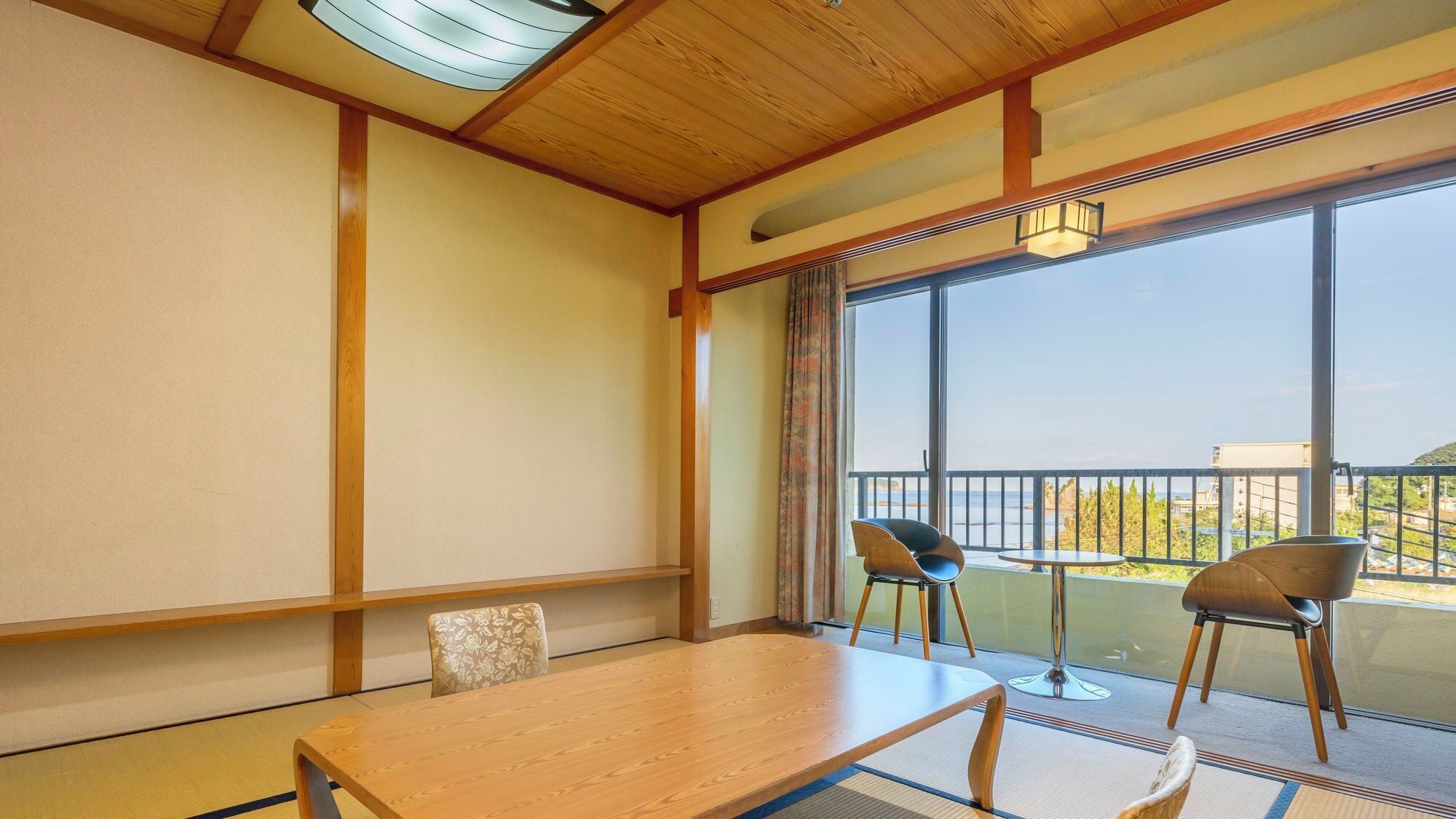 Ein Zimmer mit Holztisch, zwei Stühlen, Meerblick und einem Balkon mit Geländer.