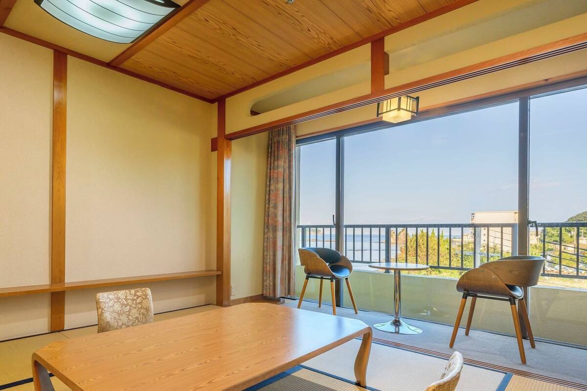 Ein Zimmer mit Holztisch, zwei Stühlen, Meerblick und einem Balkon mit Geländer.