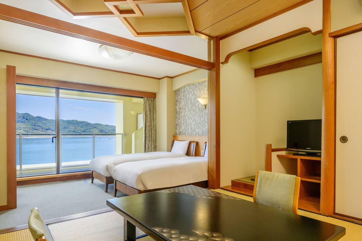 Ein Hotelzimmer mit einem großen Bett, einem Schreibtisch, einem Fernseher und Blick aufs Meer.