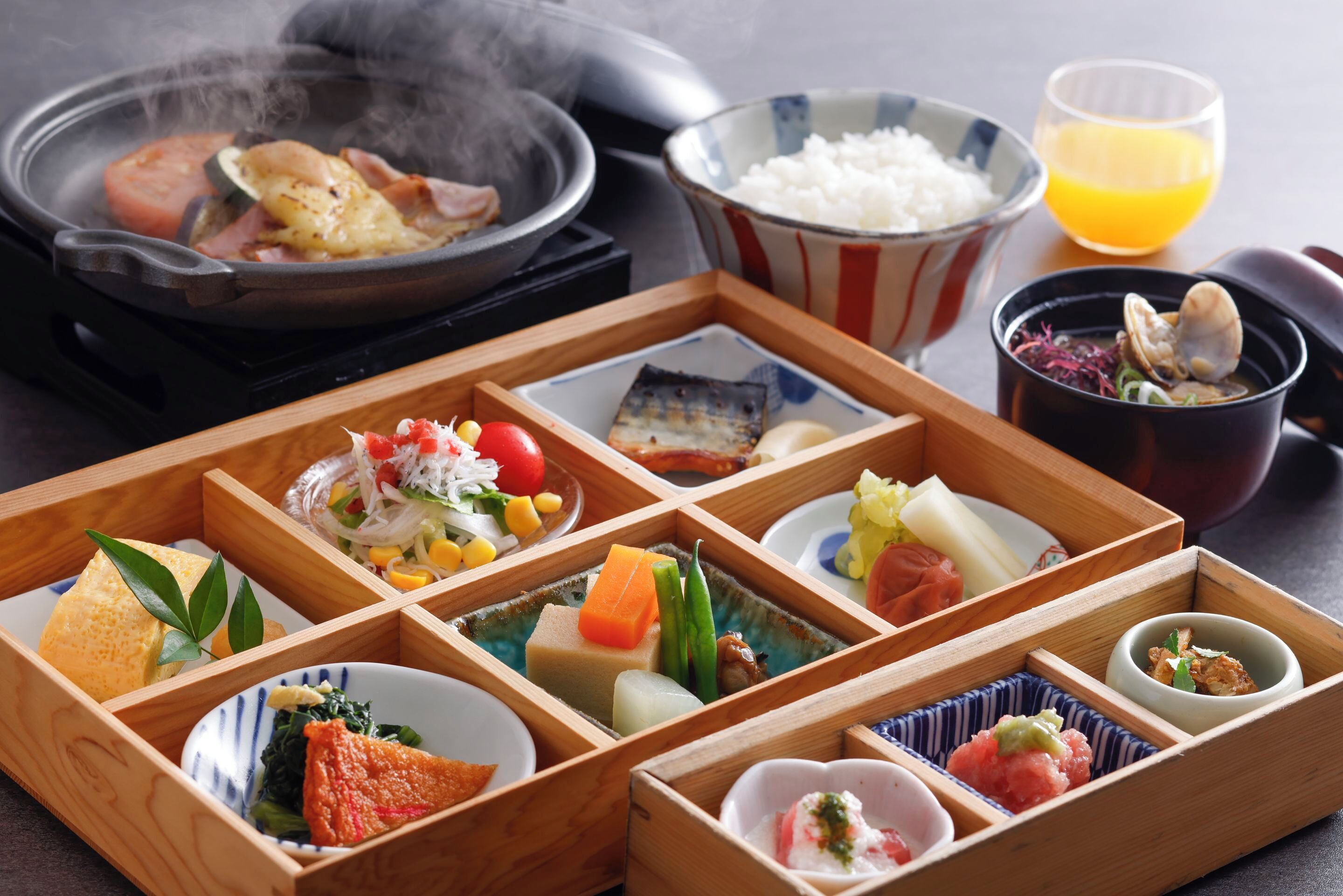 A traditional Japanese meal with various dishes in wooden boxes, a hot pot, and a bowl of rice.