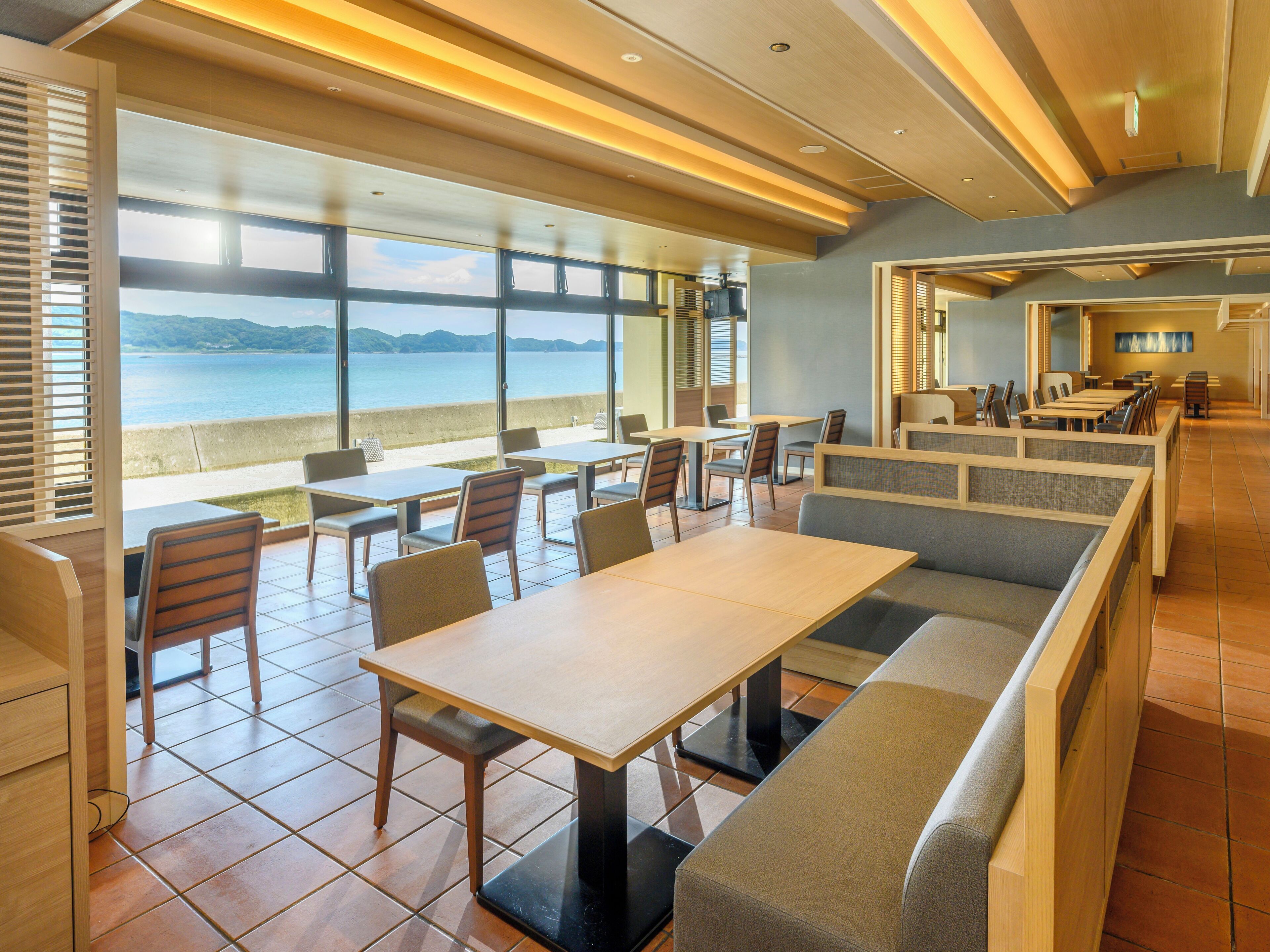 A restaurant with a view of the sea, featuring wooden tables and benches, and large windows.