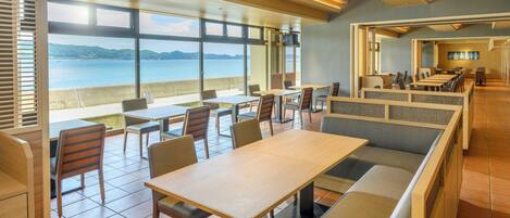 A restaurant with a view of the sea, featuring wooden tables and benches, and large windows.