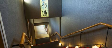 A staircase with red steps and a wooden handrail, leading to a landing with a sign in Japanese characters.