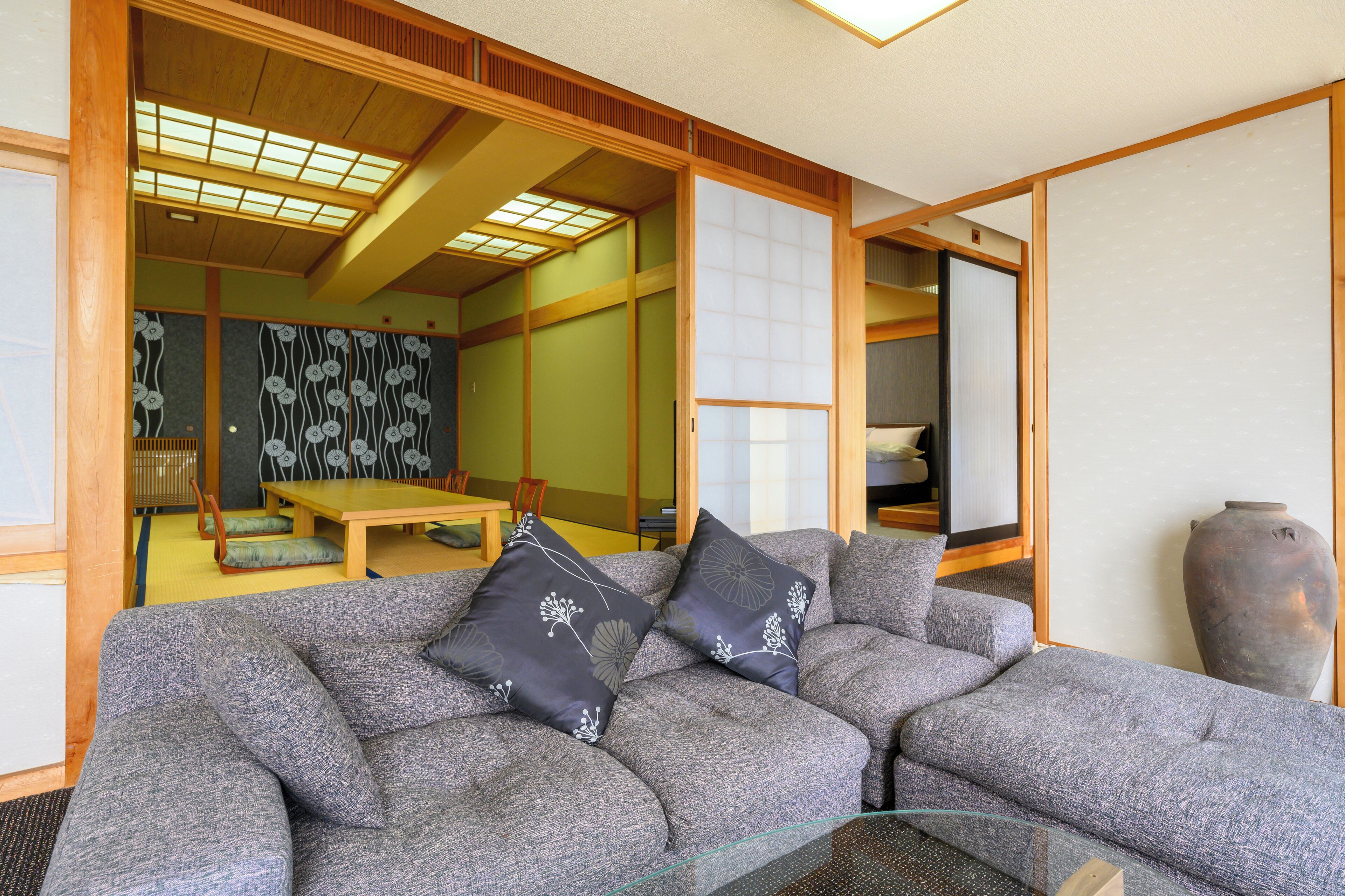 A traditional Japanese room with tatami flooring, a low wooden table, and a sofa with cushions.