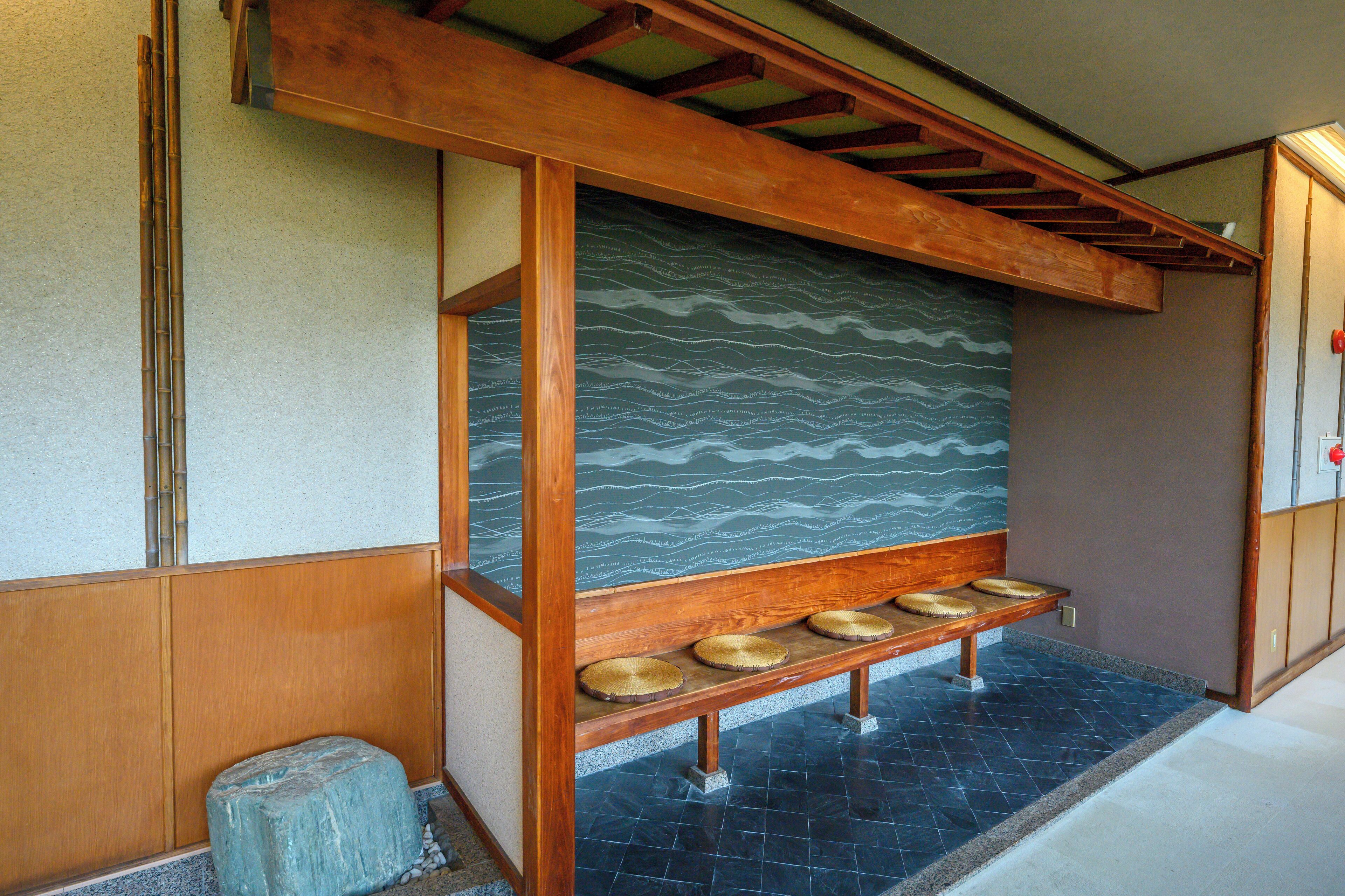 A traditional Japanese room with tatami flooring, a wooden bench with cushions, and a wave-patterned wall.