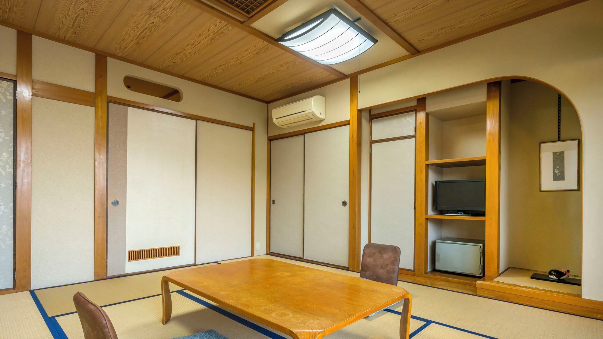 Ein traditioneller japanischer Raum mit Tatami-Boden, niedrigem Holztisch, Schiebetüren, einem Fernseher und einem kleinen Schrank.