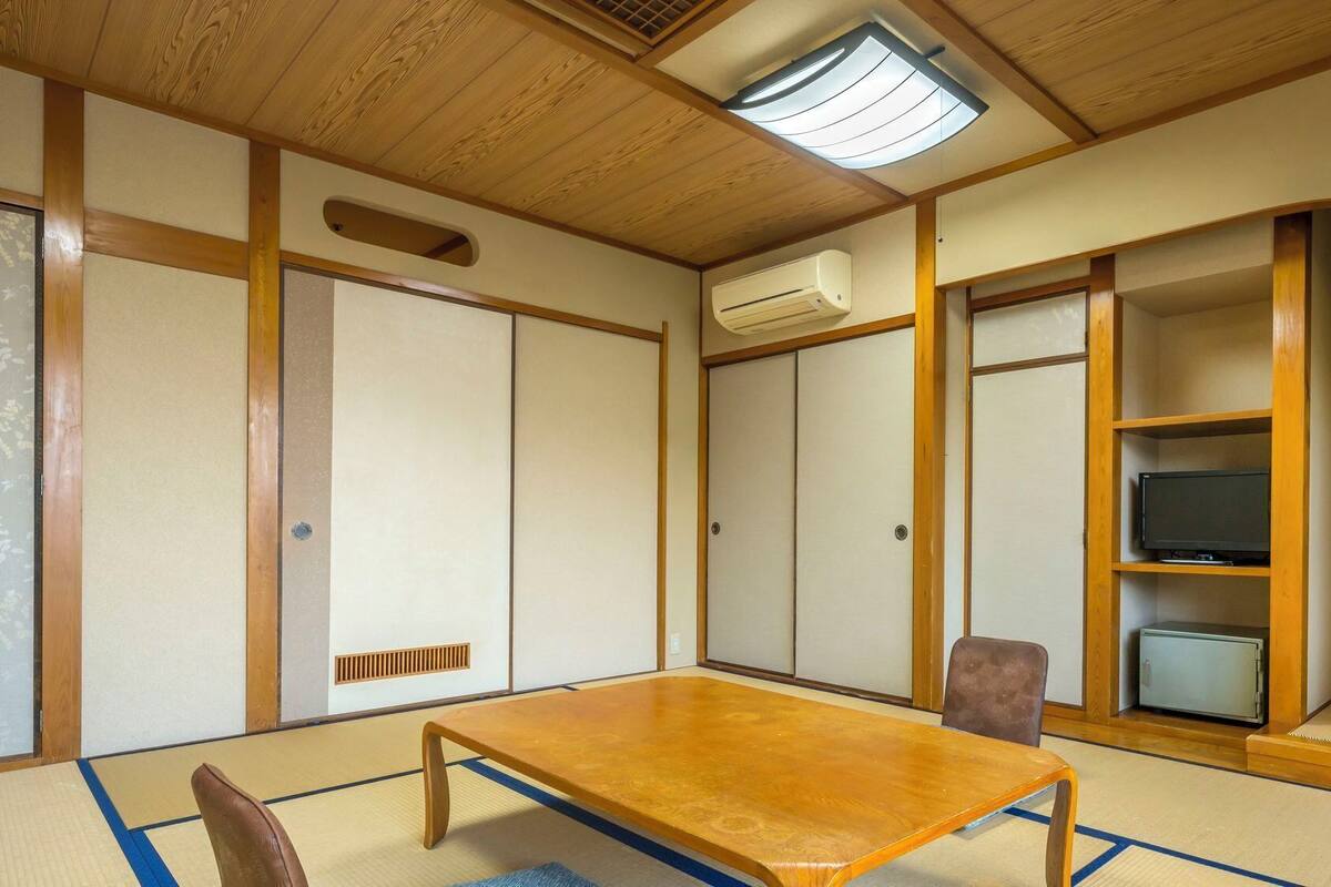 Ein traditioneller japanischer Raum mit Tatami-Boden, niedrigem Holztisch, Schiebetüren, einem Fernseher und einem kleinen Schrank.