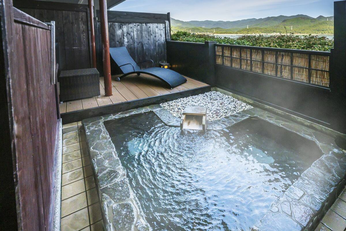Ein Whirlpoolbereich mit Holzterrasse, einer Liege und Blick auf das Meer und die Hügel.