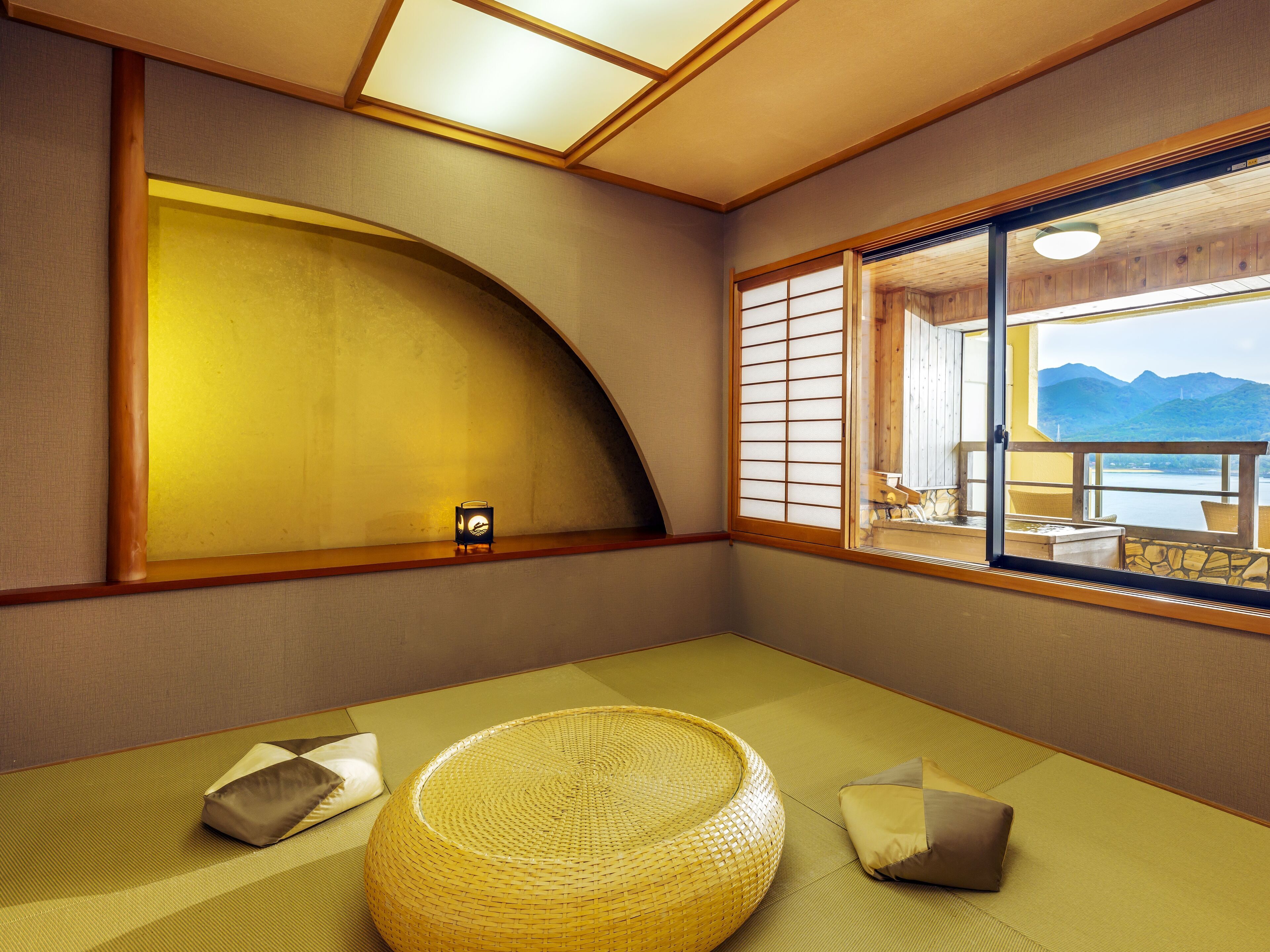 A traditional Japanese room with tatami flooring, a low wooden table, and a large window with a view of mountains.
