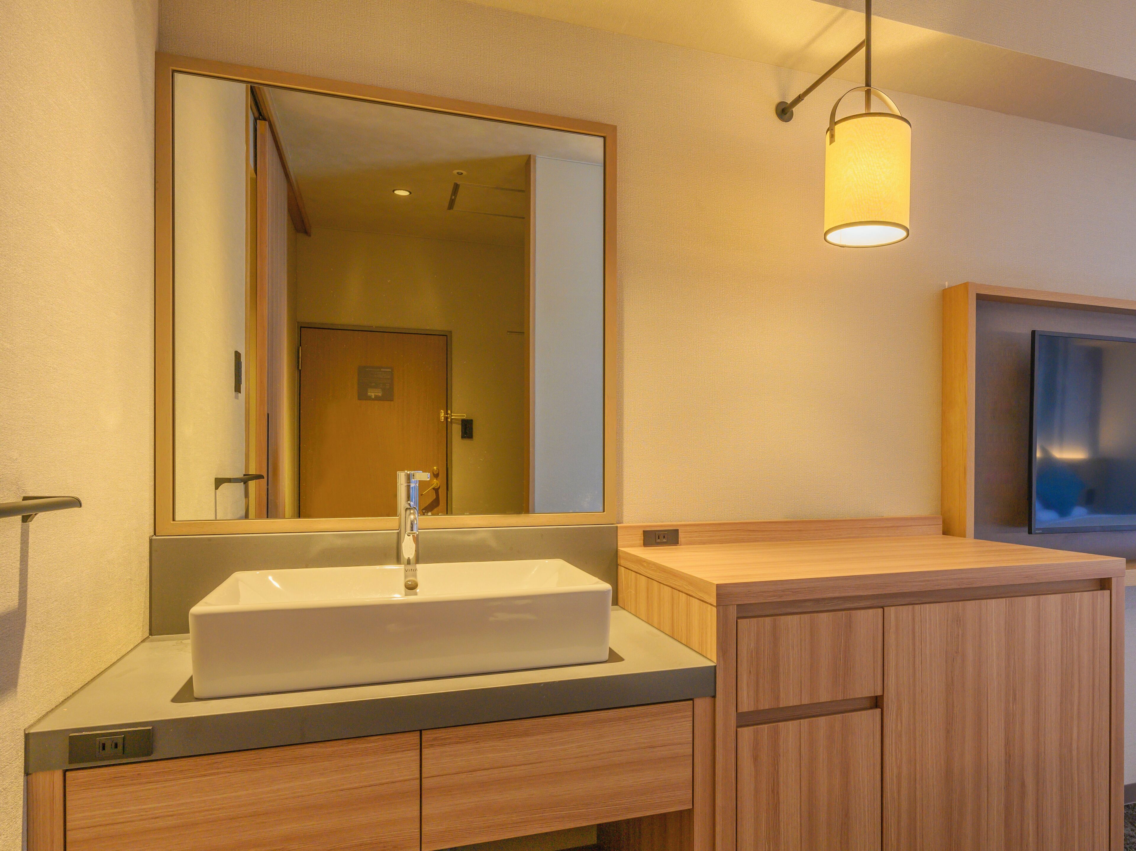 A modern bathroom with a large mirror, a sink, and wooden cabinetry.
